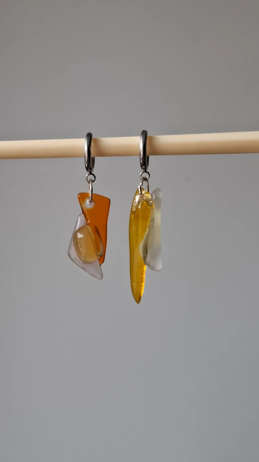 Boucles d'oreilles asymétriques en verre jaune et orange posées sur un socle en bois brut