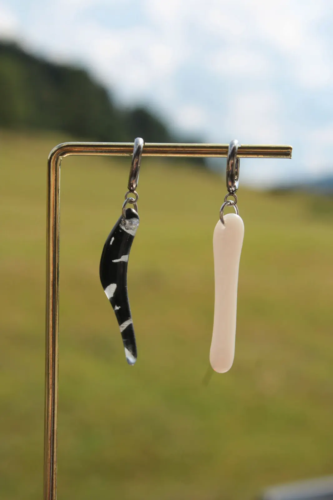 Boucles d'oreilles pendantes asymétriques en verre noir marbré et blanc suspendues à un présentoir.