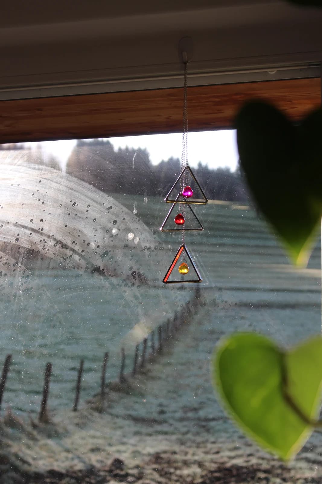 Attrape-soleil en vitrail composé de triangles suspendu devant une fenêtre face à la nature