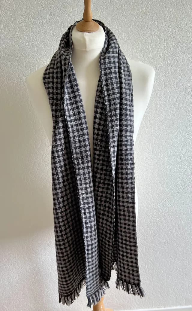 Écharpe à motif quadrillé noir et blanc et franges, drapée sur un buste de mannequin blanc.