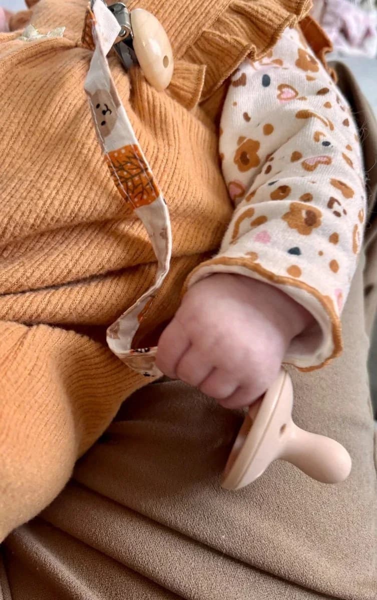 Ruban attache-tétine en tissu à motifs automnaux relié à une tétine sur un plaid écru
