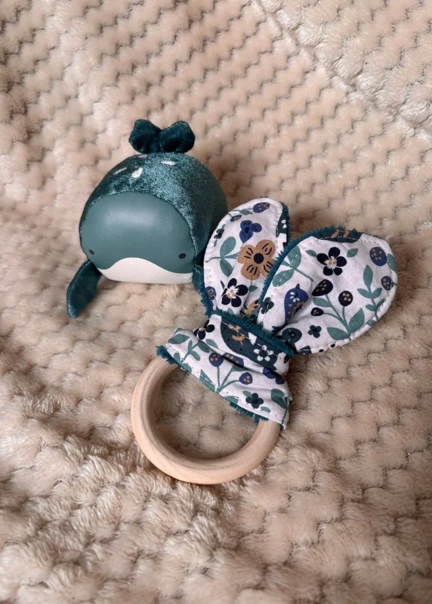 Anneau de dentition en bois avec tissu oreilles de lapin à motifs végétaux bleu canard sur plaid doux.