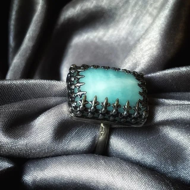 Bague en argent ornée d'une calcite bleue rectangulaire posée sur un tissu satiné gris plissé