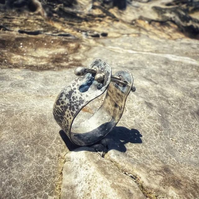 Bague large en métal argenté martelé avec tiges mobiles, posée verticalement sur une roche claire.