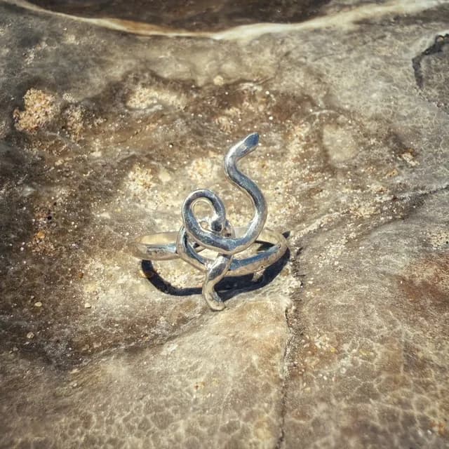 Bague en argent aux formes ondulées et entrelacées posée sur une roche texturée.