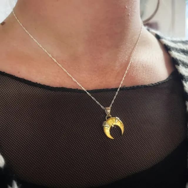 Collier avec pendentif lune en laiton et argent porté au cou sur une chaîne fine torsadée.