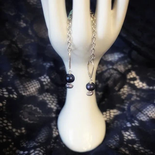 Boucles d'oreilles pendantes en argent avec perles sombres irisées, sur un présentoir main.