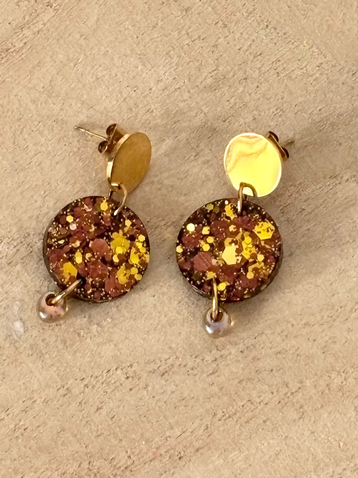 Paire de boucles d'oreilles pendantes rondes marron pailleté et doré sur support blanc.