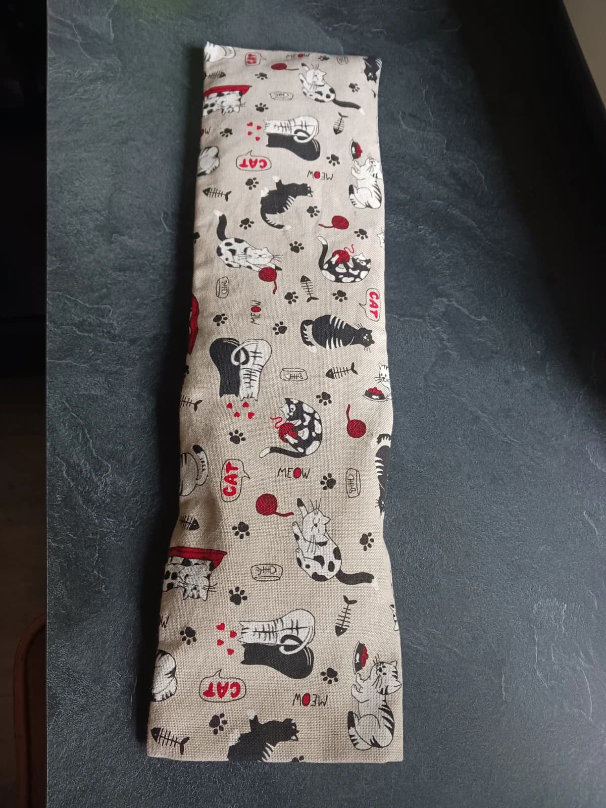 Bouillotte longue en tissu beige imprimé de chats noirs et blancs avec pelotes de laine rouges