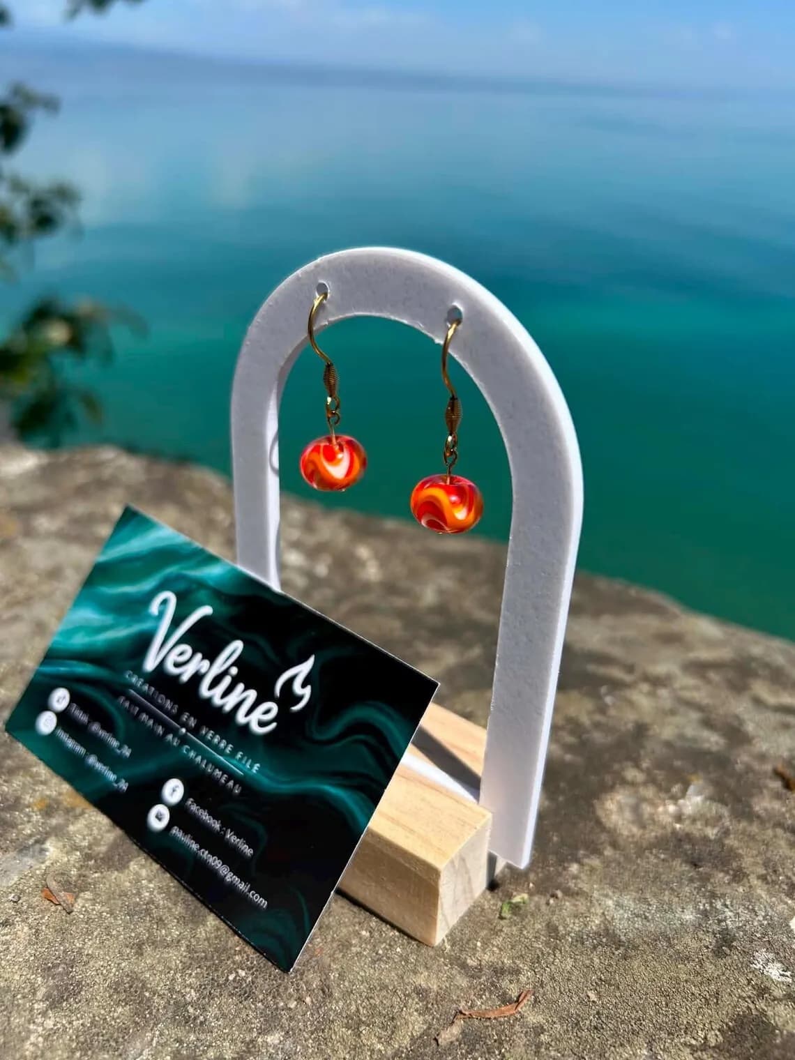 Boucles d'oreilles pendantes avec perles marbrées orange et dorées sur un présentoir arche blanc.