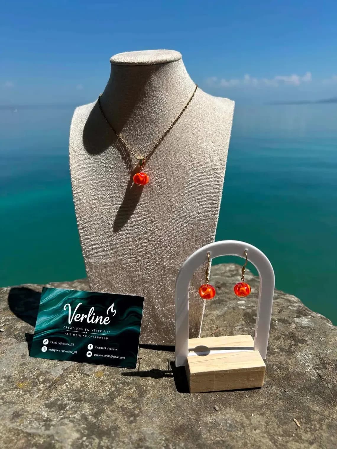 Parure collier et boucles d'oreilles en verre filé orange et doré exposée face à l'eau