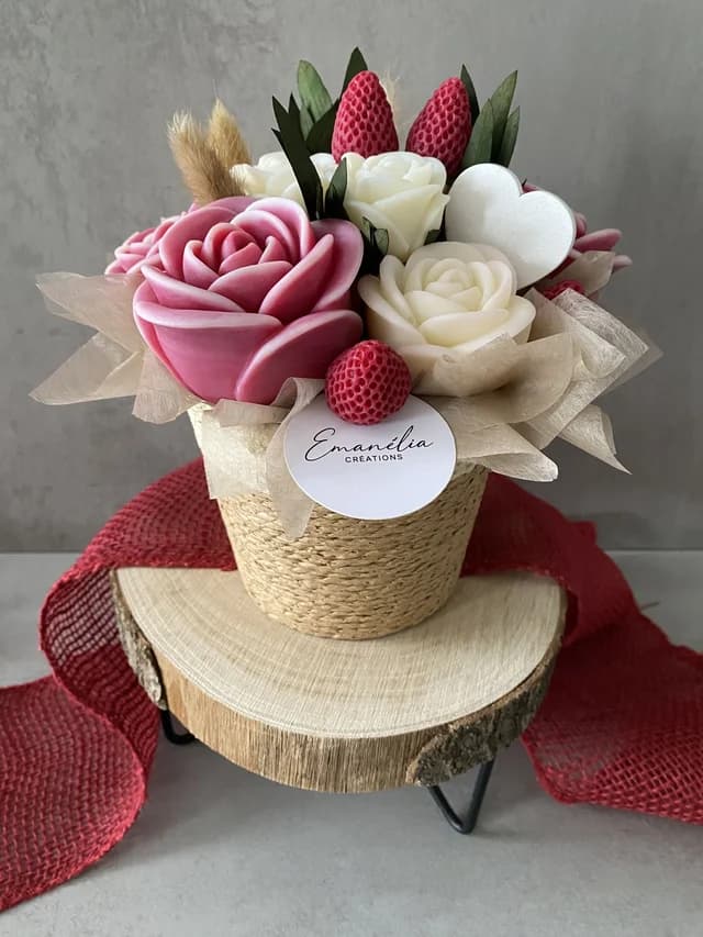 Bouquet décoratif aux roses roses et blanches avec fraises dans un pot tressé posé sur un rondin de bois.