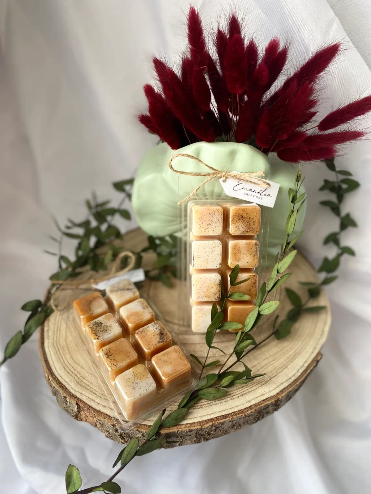 Deux tablettes de cire parfumée aux teintes caramel et crème présentées sur un rondin de bois avec feuillage.